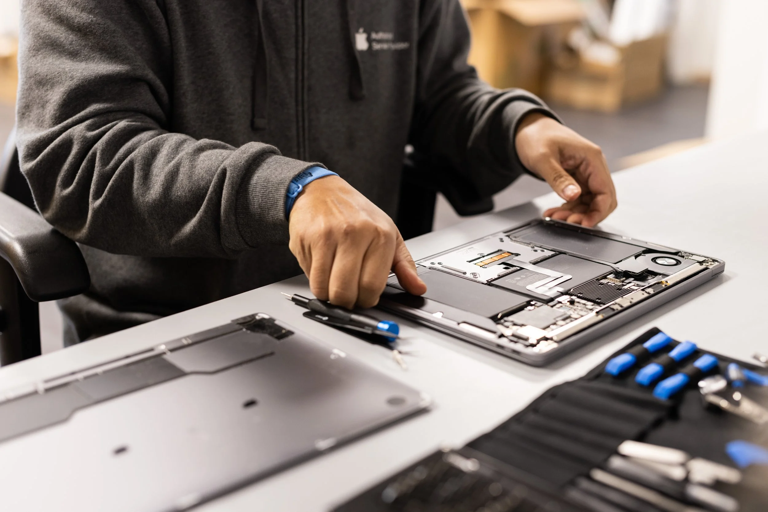 A technician opening a MacBook for repair at Compco USA, an Apple Authorized Service Provider